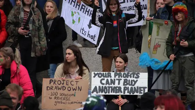 A group of young women protestors with placards, one reading "Your profits can't buy another planet"