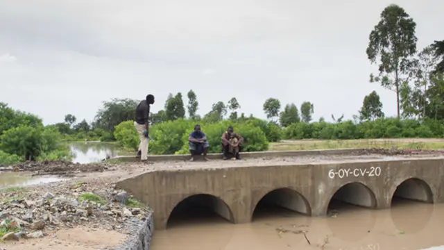 Three men stand on a bridge over an open culvert
