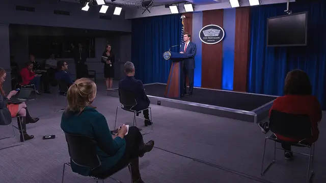 People sit on chairs two metres apart while listening to a man at a lectern