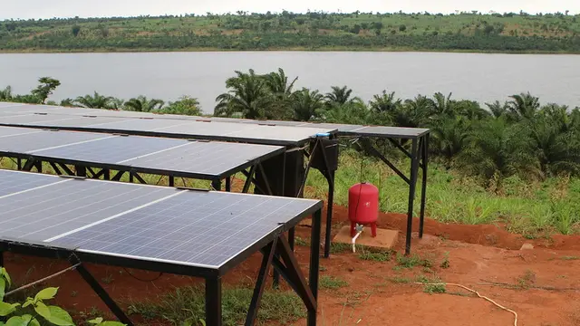Solar panels on the ground next to a lake.