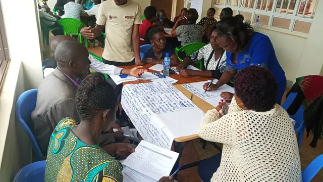 Men and women sitting around a table, writing on poster-like papers