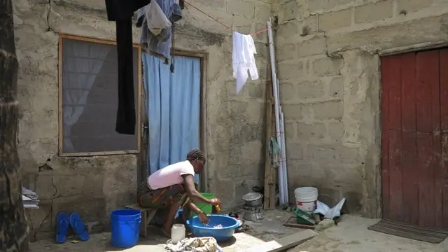 Woman washing dishes in a bowl outside.