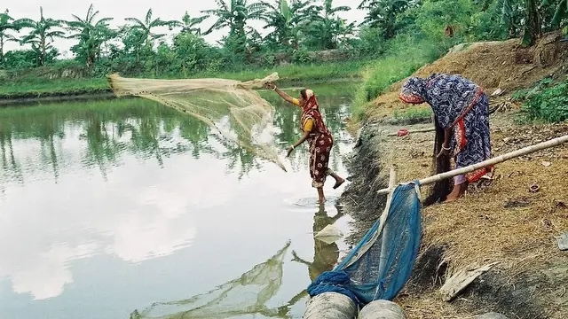 Two women throwing fishing nets at a lake 