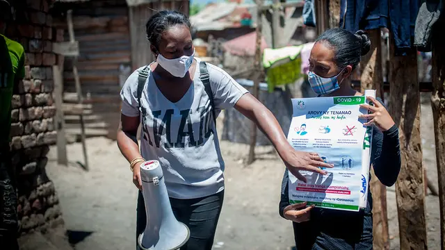 A woman holds a poster with instructions. Another one holds a loudpseaker and points at a poster.