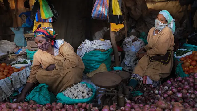 Women sit next to piles of vegetables like onions, tomatoes, garlic.