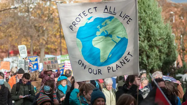 People of all ages marching holding posters. One poster reads "protect all like on our planet"; another poster reads "no more blah blah blah"