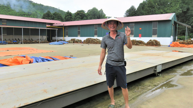 A Vietnamese man poses in front of buildings and piles of timber