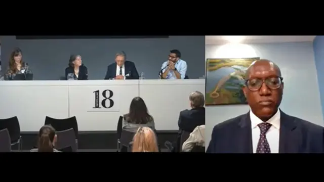 On the left, a panel of 4 people siting on a table with microphones. On the right, a man on a videocall.