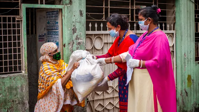 Two women wearing masks hand over a bag to another woman wearing a mask