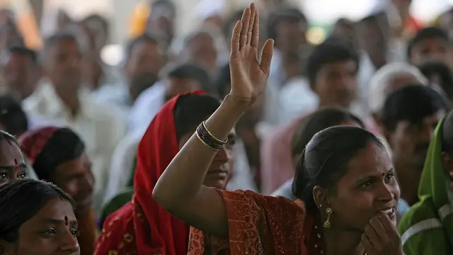A woman in a crowded room raises her hand to speak.