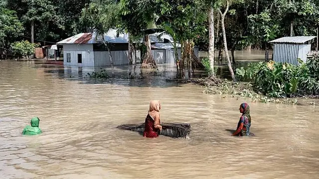 Three women try to walk while almost completely submerged in flood water. 