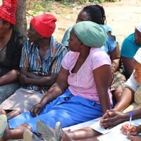 Group of women sitting on the gournd and looking to the left.
