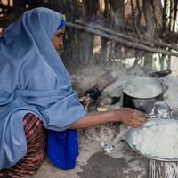 Woman sitting on a stool prepares rice from a pot.