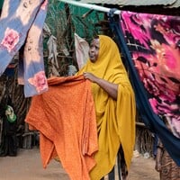 A woman hols a piece of clothes looking at a drying line.