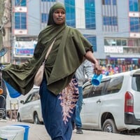 Woman holding a plastic cup walks on the street.