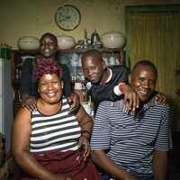 A family of four sit at home smiling at the camera. 
