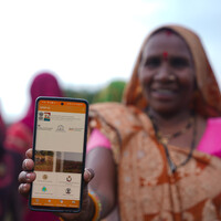 Woman wearing a sari smiles and shows a phone to the camera.