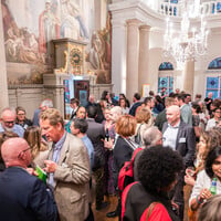 A large group of people talk and laugh in an open space. 