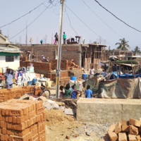 Image of fishing community slum of Sai Baba Sahi during construction, showing building materials and people working.