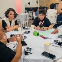 People sitting down at a round table, discussing and writing down ideas.