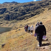 People walk along a hillside above a lake.