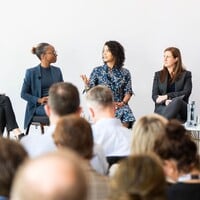 Panel of speakers sitting on chairs on a stage, taking, while the audience listens.