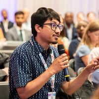 Audience member sitting down and asking a question, speaking into a microphone.