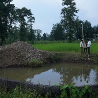 Three men stand beside a well that looks in a state of disrepair. 