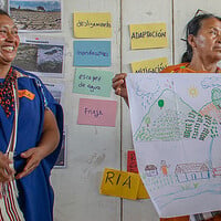 Two woman hold up large sheets of paper on which is writing and diagrams. 