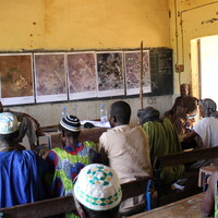 people sit as desks looking forward at photos pinned on a wall.